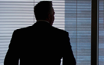 A man in a suit looking out the blinds